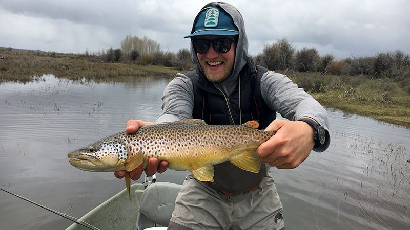 man holding brown trout while fly fishing in jackson hole